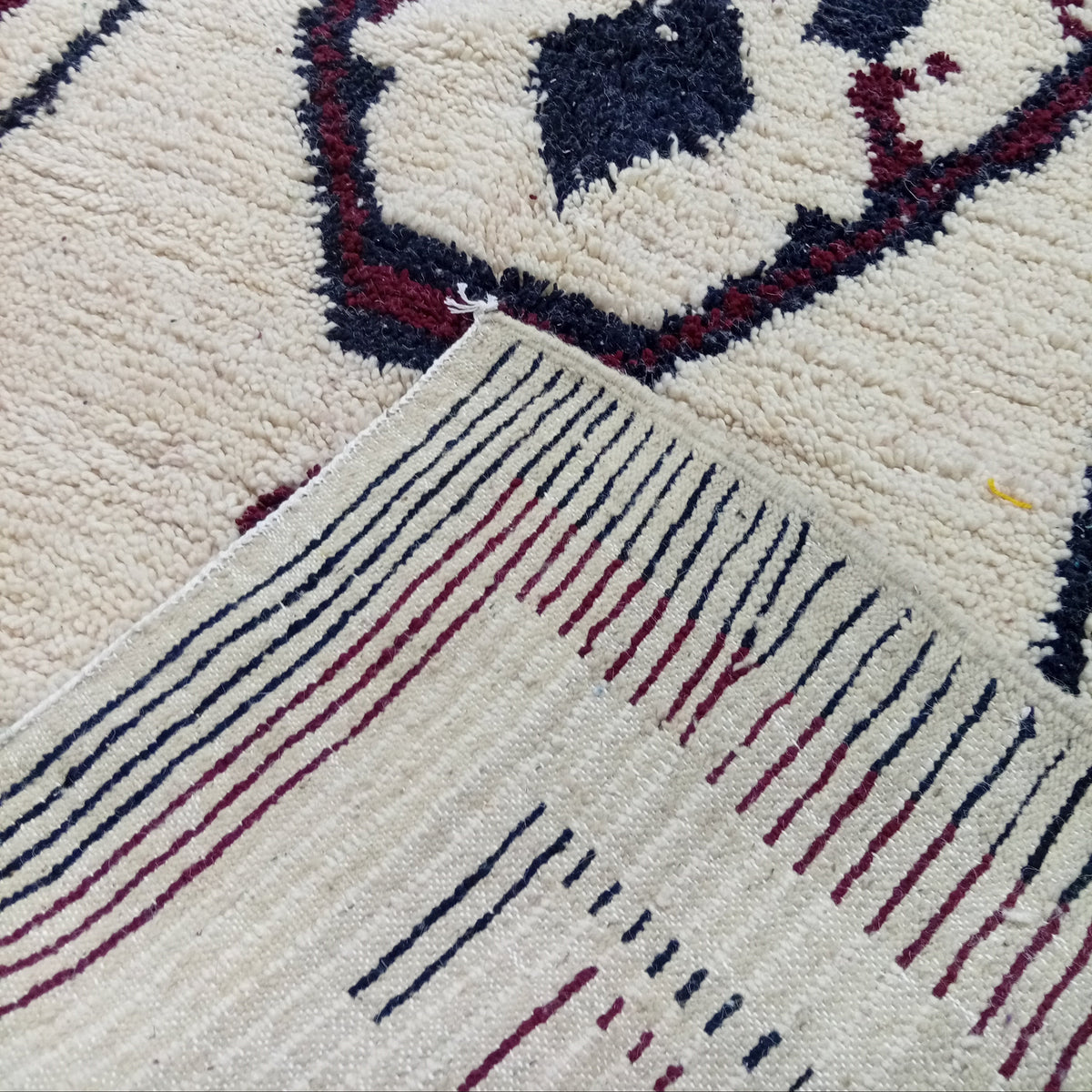 A close-up of a textured area rug with a cream base, featuring a geometric medallion pattern in dark navy blue and burgundy red, with a striped border.